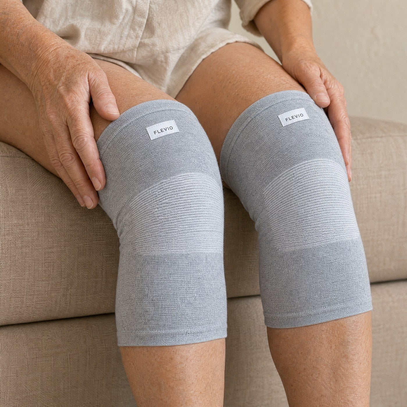 Genouillères de compression grises portées assise, mains posées sur les genoux